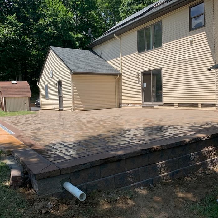 Newly installed brick paver patio with a raised retaining wall beside a beige house.