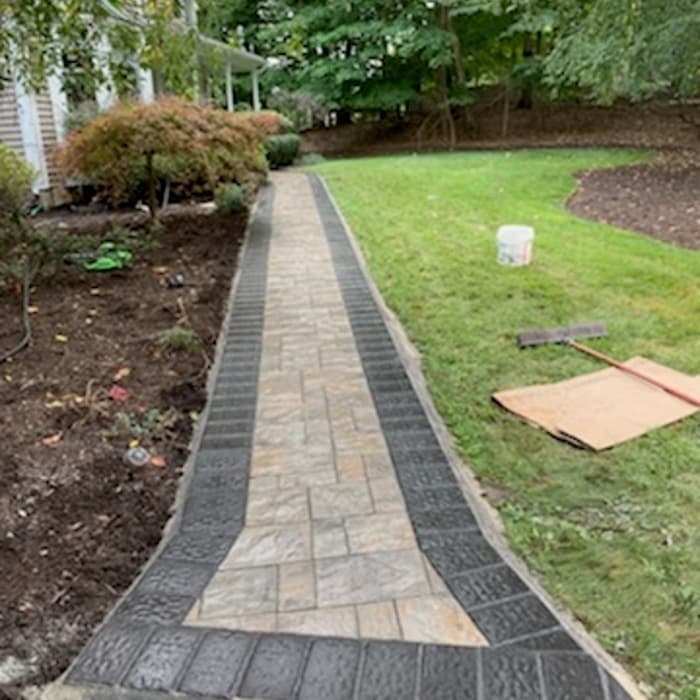 New stone paver walkway with dark border edging installed through a landscaped yard.