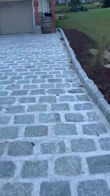 A wide natural stone paver driveway installed in front of a house and garage.