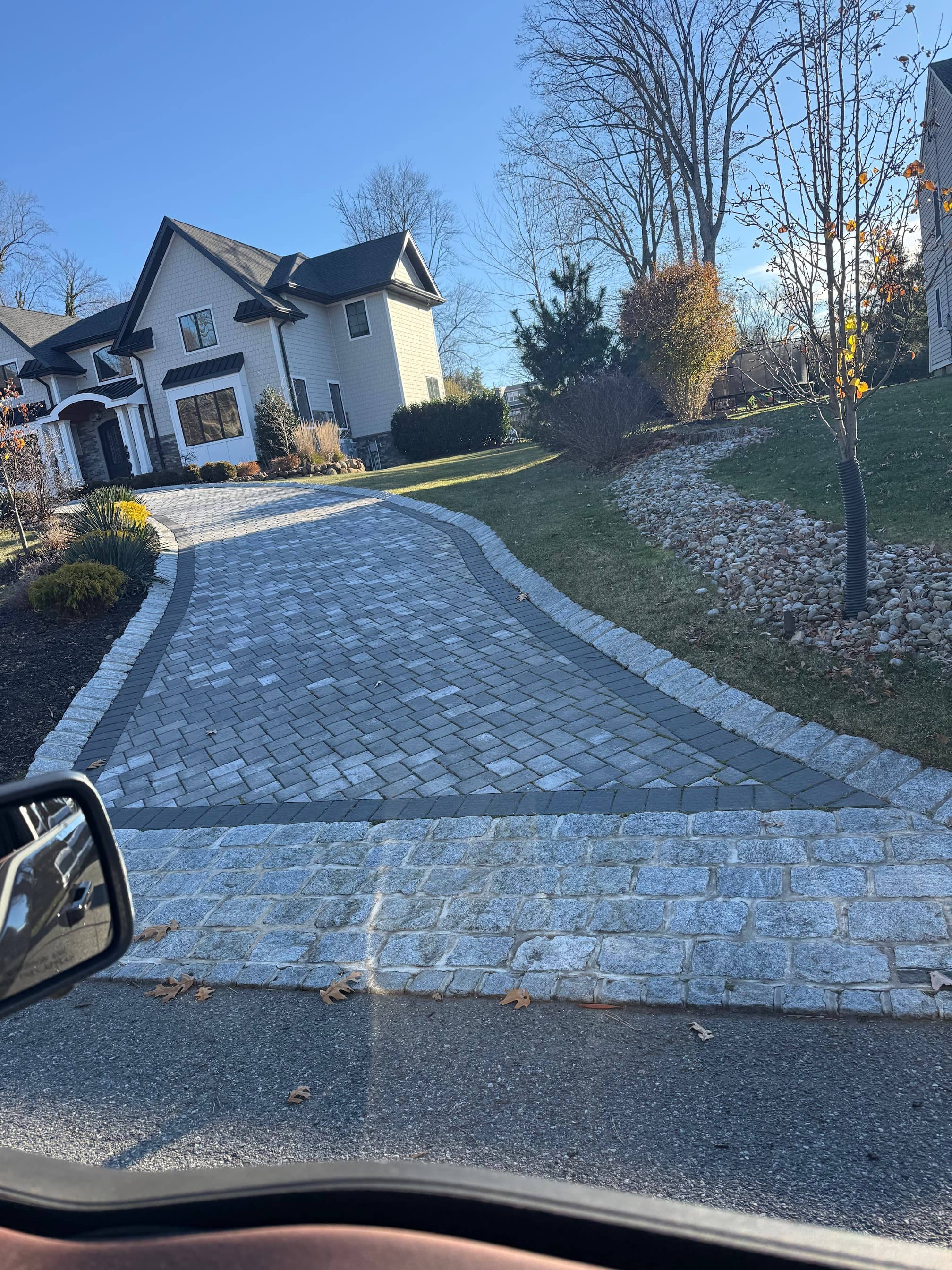 Curved gray paver driveway with stone edging leading to a large suburban home.