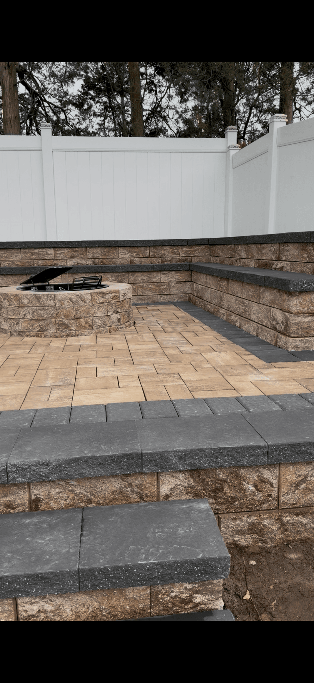 Backyard patio with stone retaining walls, pavers, and a circular fire pit.