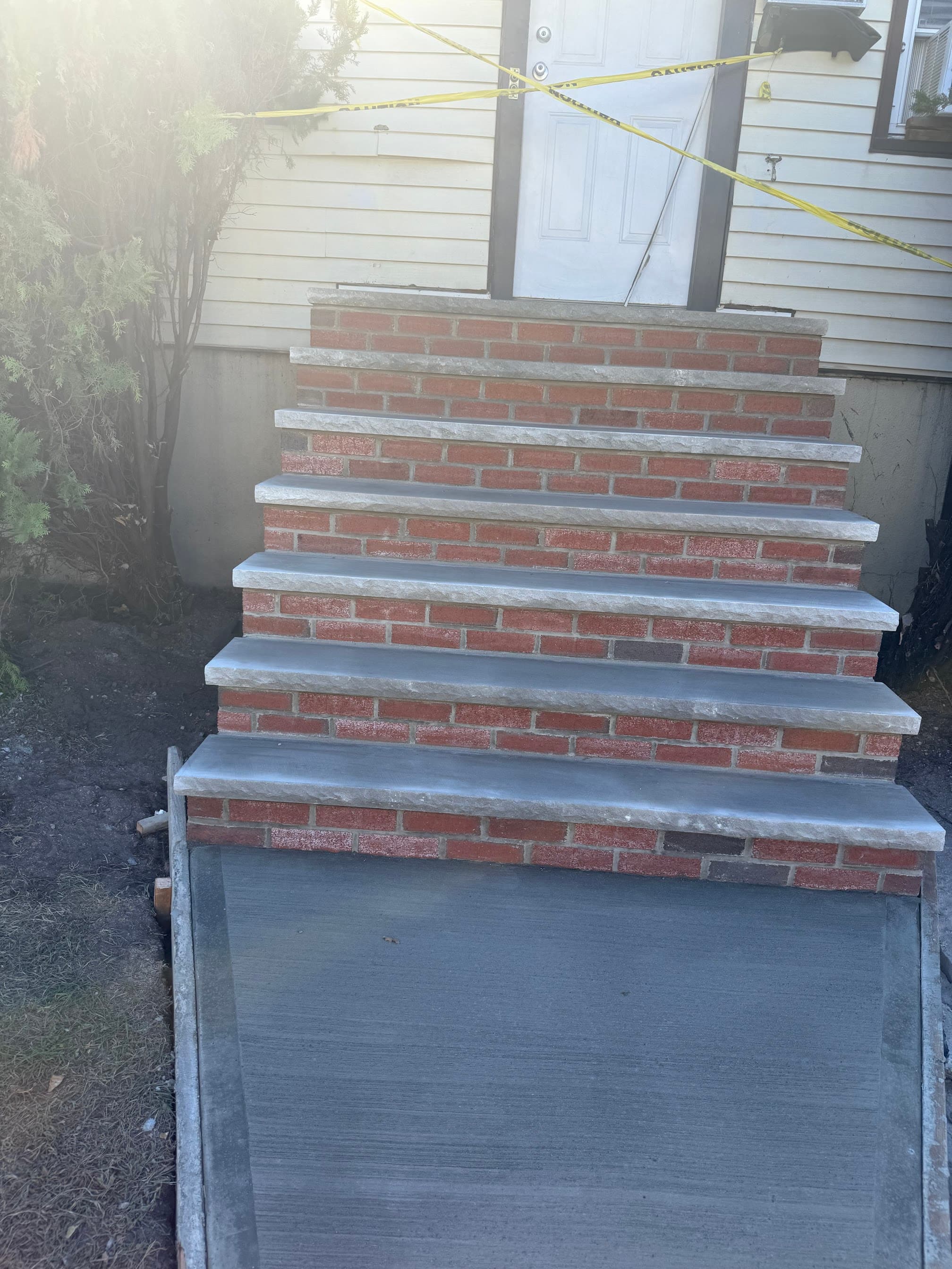 New brick front steps with concrete treads leading to a taped-off house entry.