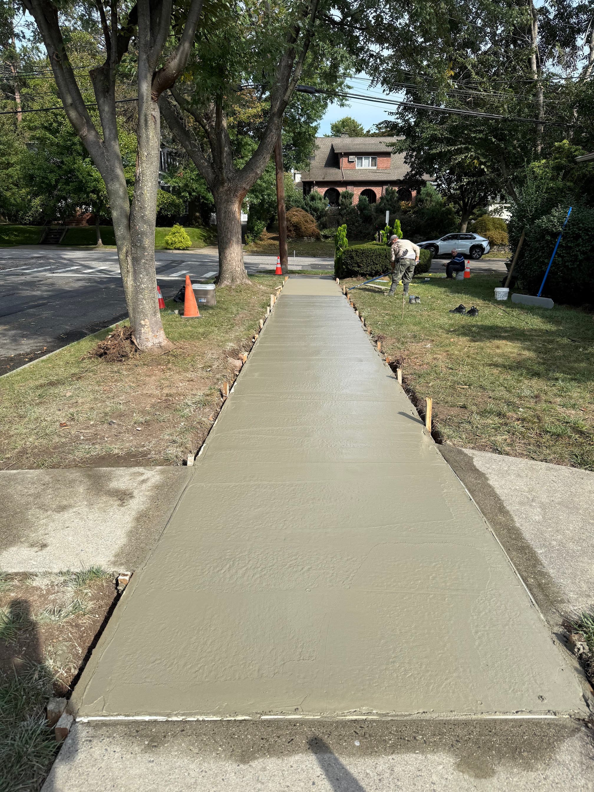 Workers finishing a newly poured concrete sidewalk in a residential yard.