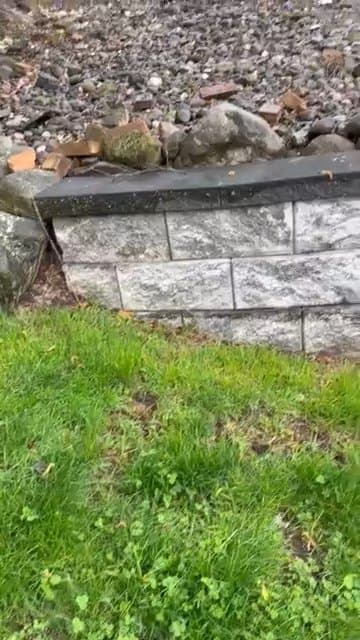 Gray natural stone retaining wall with a dark cap beside a grassy slope.