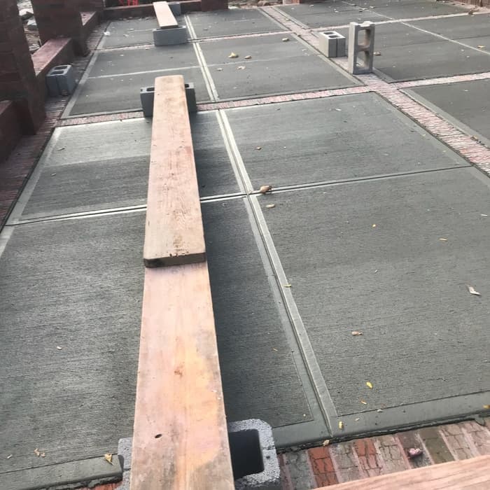 Fresh concrete slabs under construction with wooden planks and cinder blocks laid across the surface.
