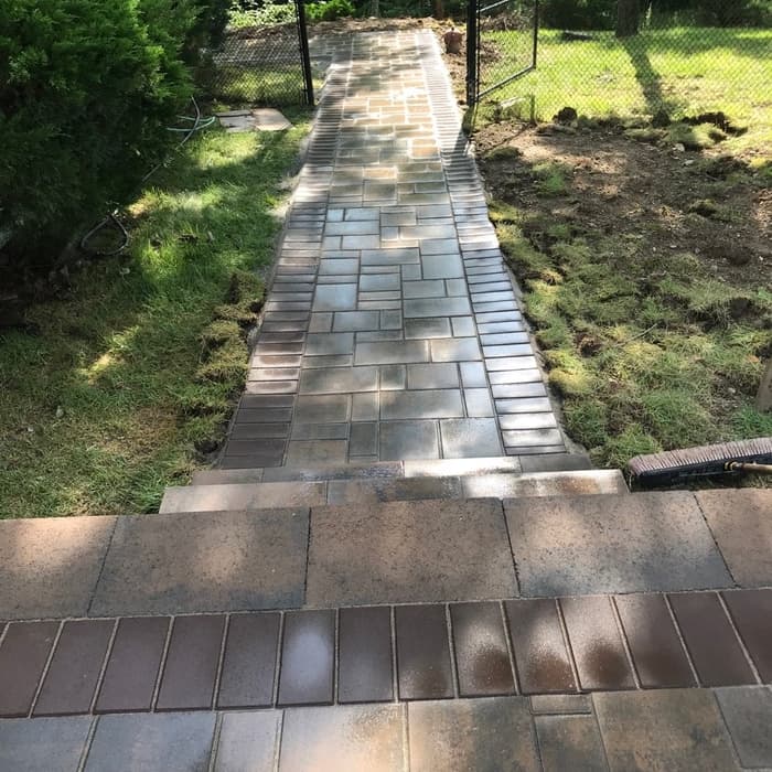 New brick paver walkway with border edging leading through a landscaped yard.