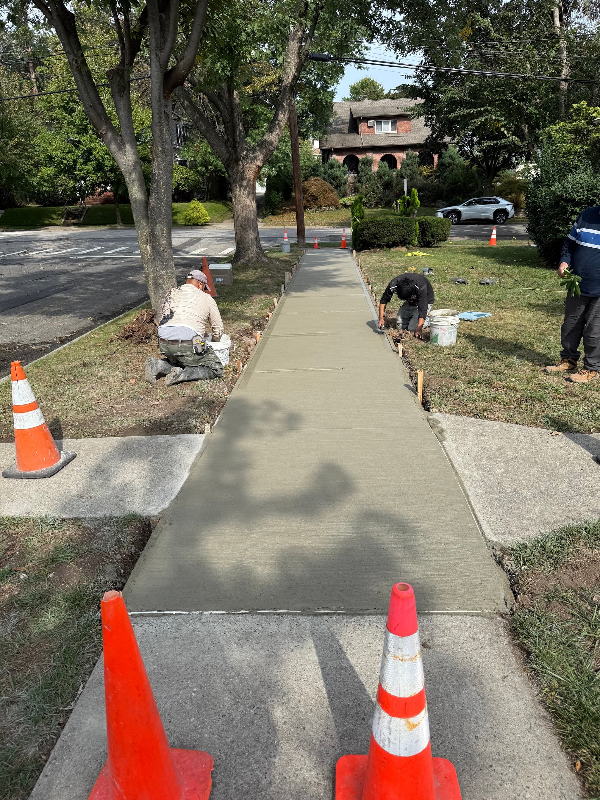 Workers finishing a freshly poured concrete sidewalk on a residential street.
