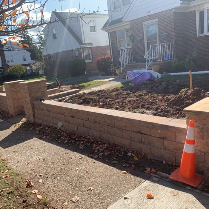 New tan stone retaining wall bordering a front yard garden in front of a house.