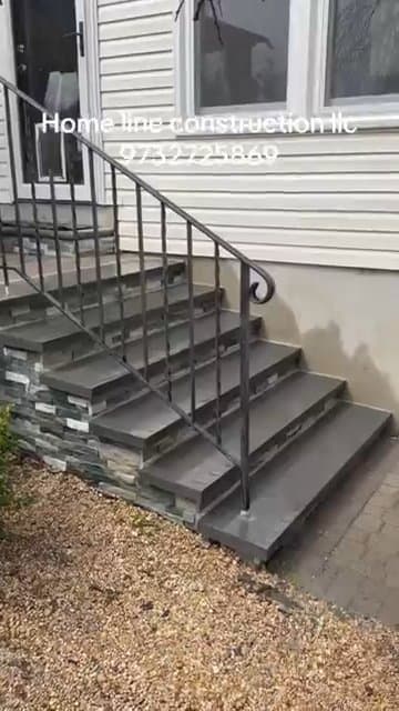 Front steps and retaining wall finished with stacked stone veneer and black metal railings.