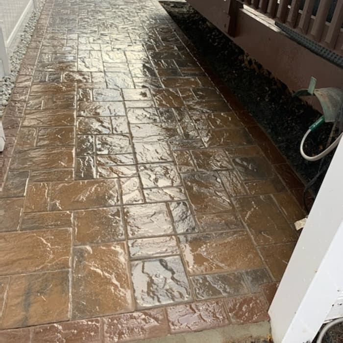 Freshly cleaned stamped concrete walkway beside a deck with a wet, glossy finish.