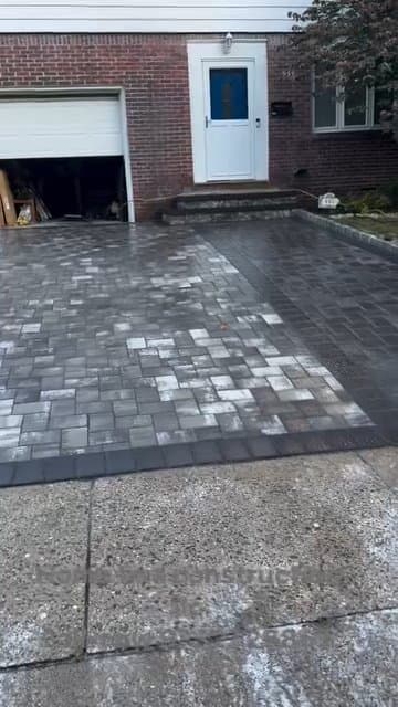 New gray paver driveway installed beside a brick house and garage.