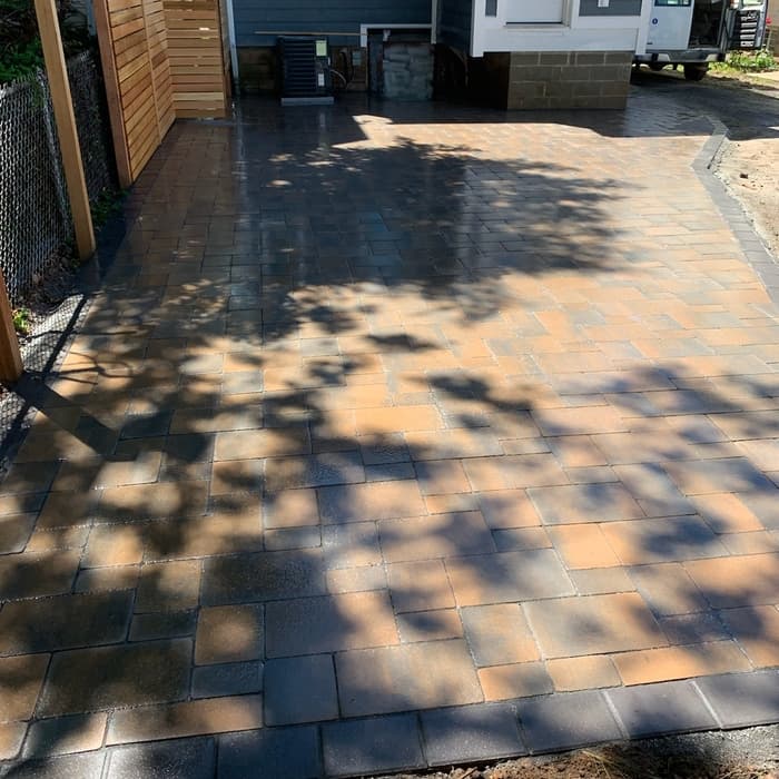Newly installed interlocking paver driveway beside a house with mixed earth-tone bricks.