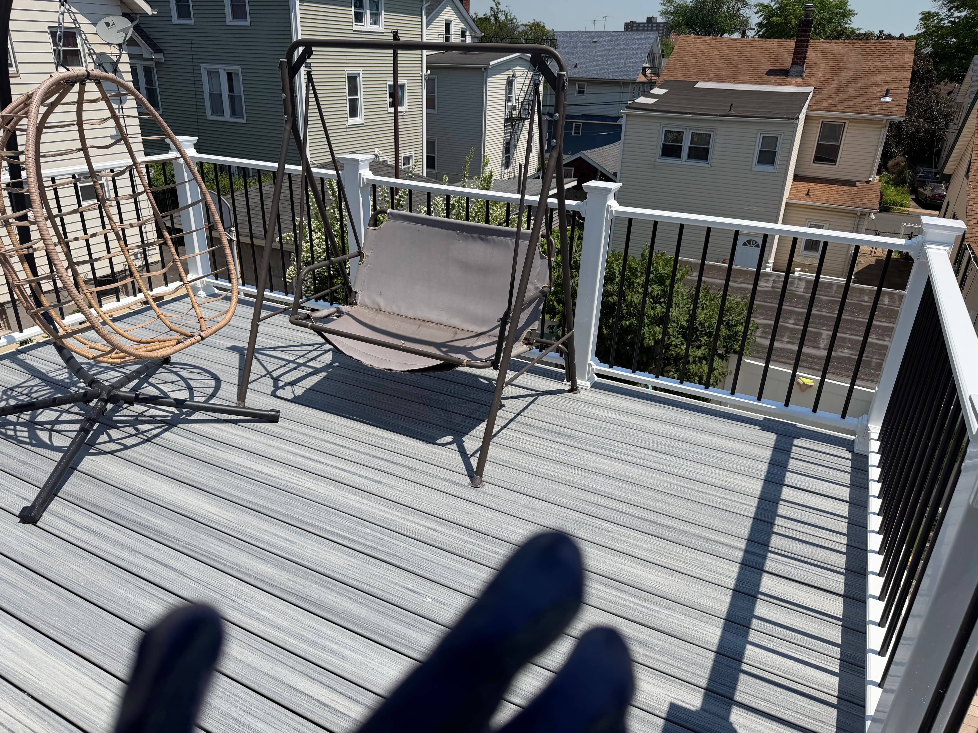 Finished elevated deck with gray decking, white railings, and hanging chairs overlooking nearby houses.