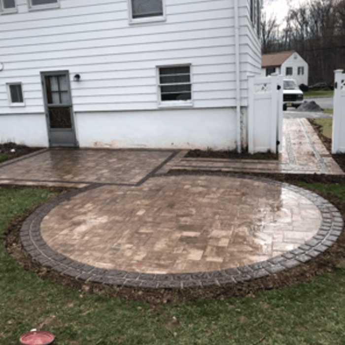 Circular brick paver patio with matching walkway installed beside a house.