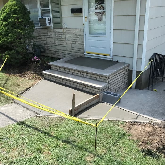 Freshly poured concrete front porch and walkway with brick steps at a home entrance.