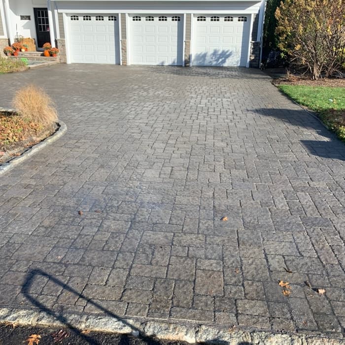 Gray interlocking paver driveway leading to a three-car garage at a residential home.