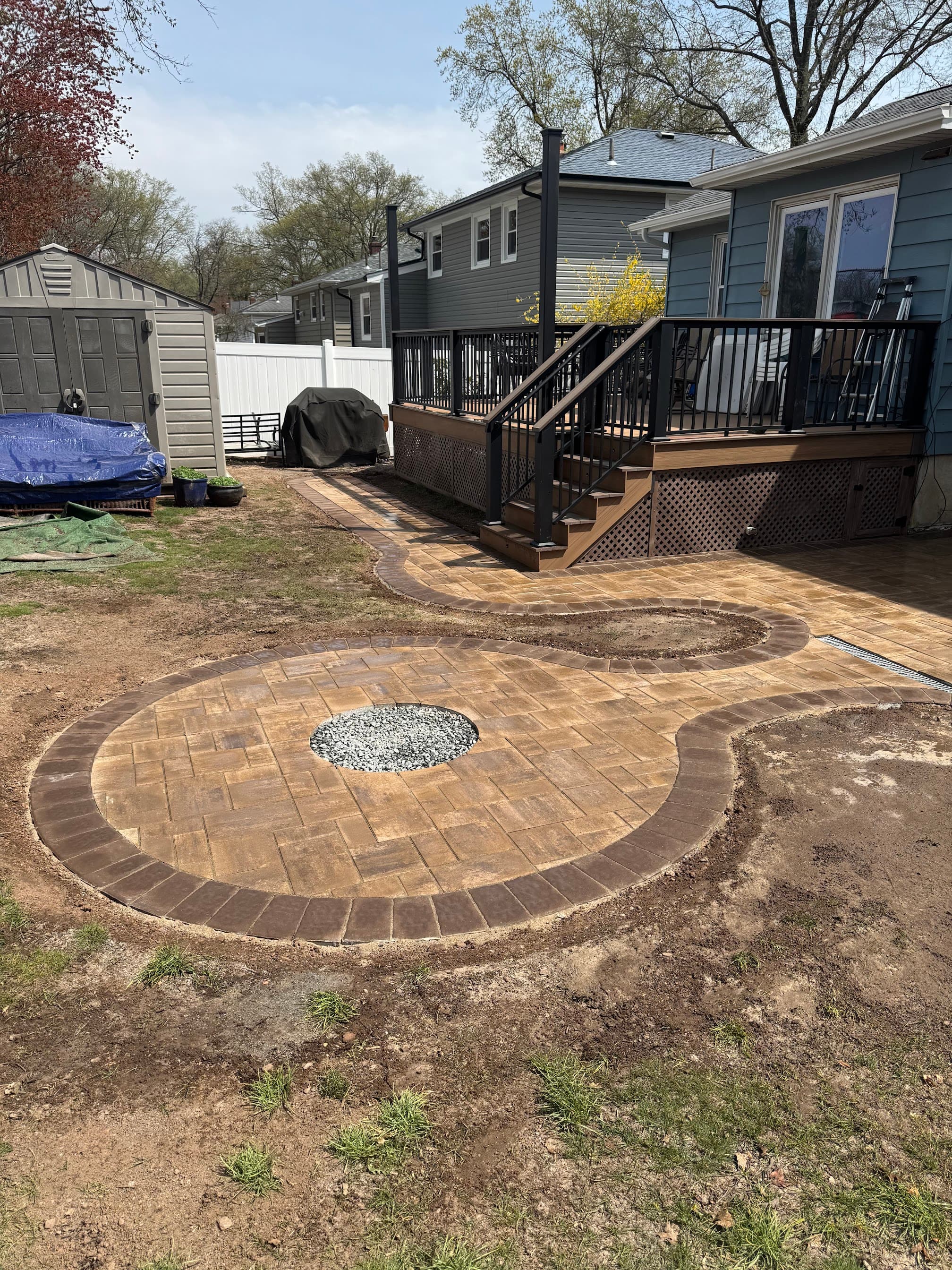 New backyard paver patio with circular design and curved walkway beside a residential deck.