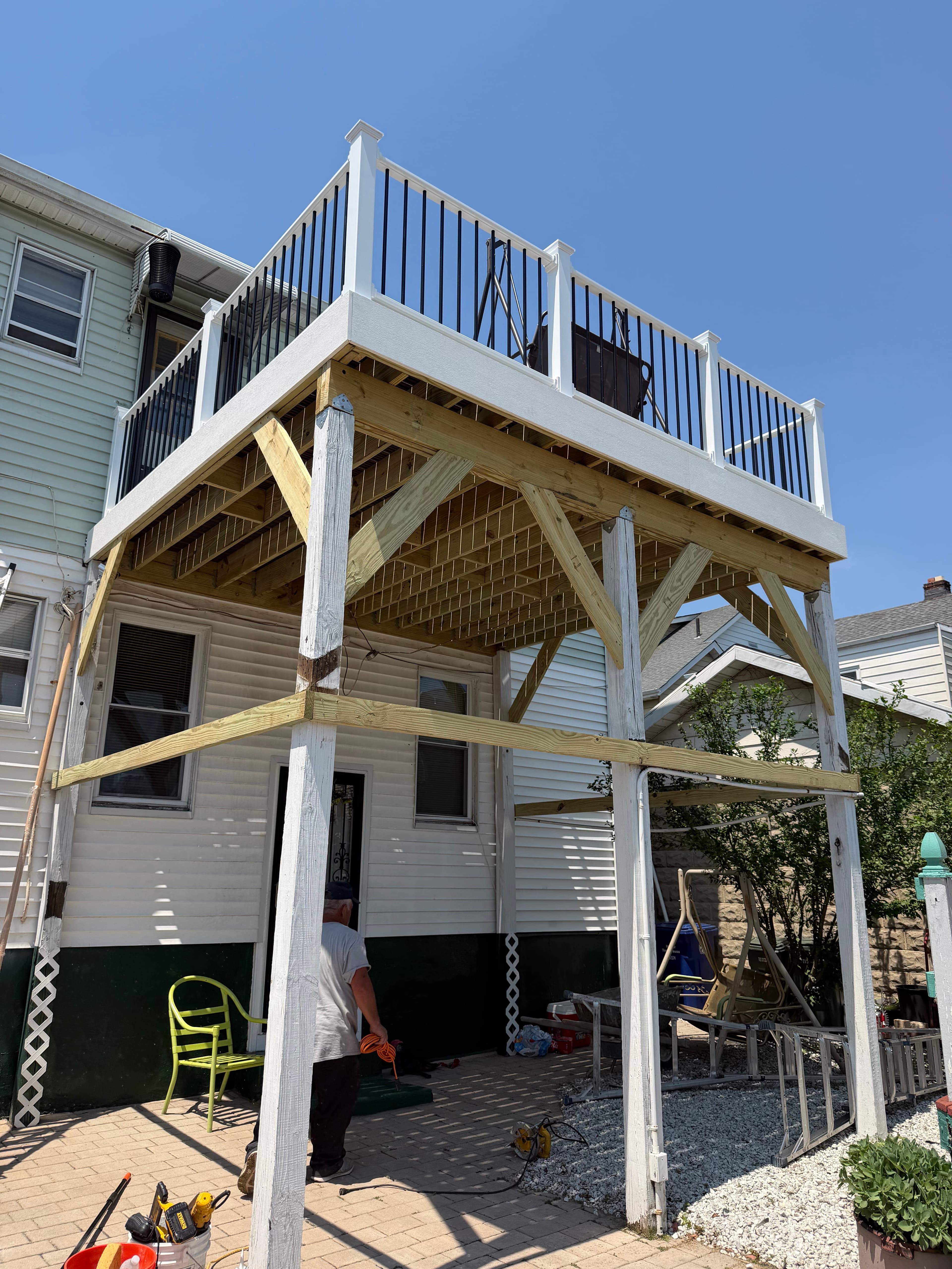 Raised backyard deck under construction with wood framing and white-and-black railings.