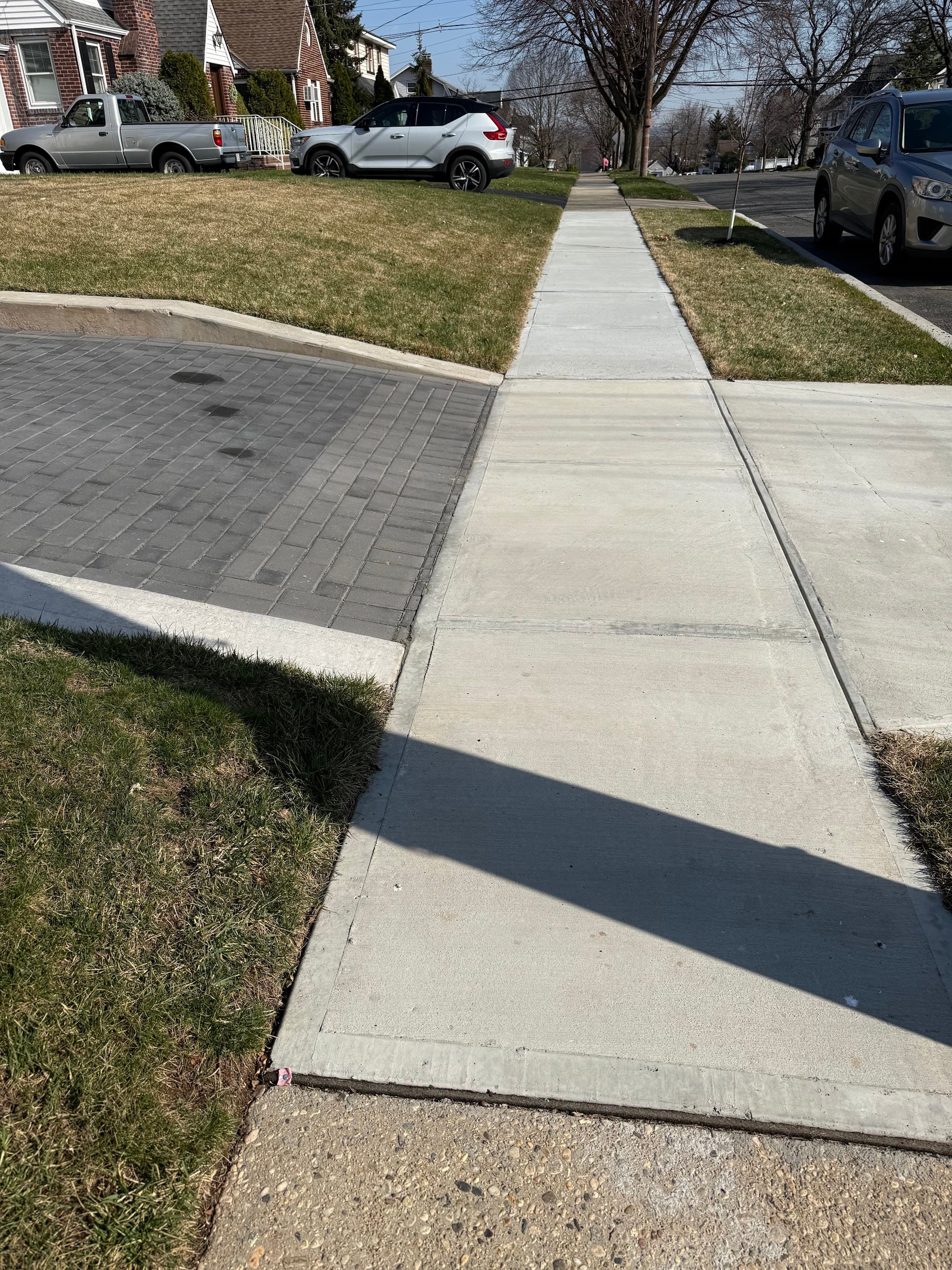 New concrete sidewalk and driveway apron beside a residential lawn and paver driveway.