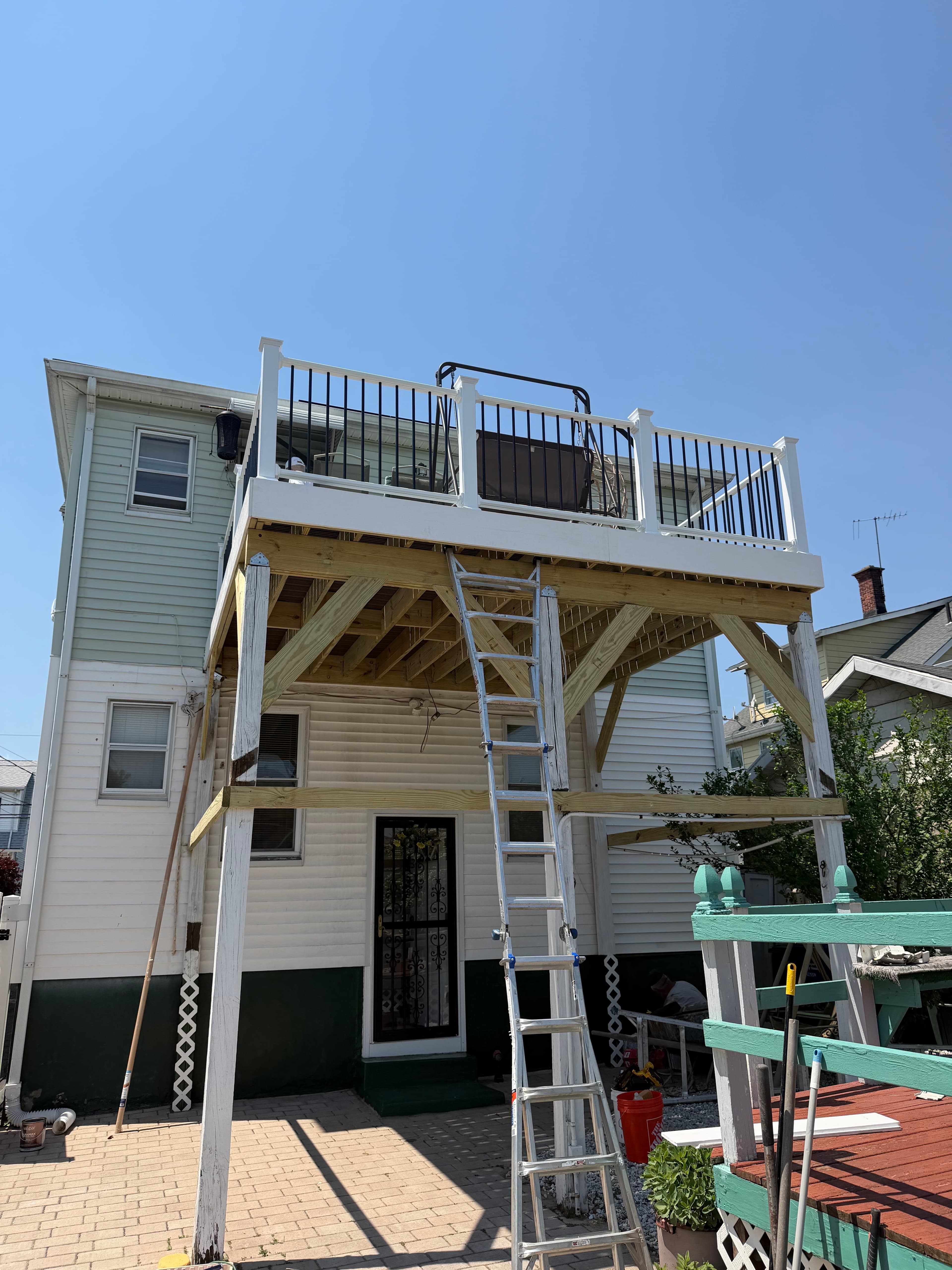 Raised deck under construction with new framing, posts, and white railings on the upper level.