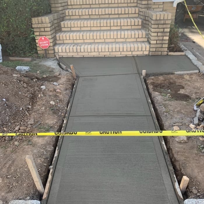 Freshly poured concrete walkway under construction leading to brick steps.