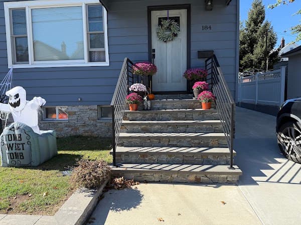 Residential front stoop with stone steps, black railings, and potted flowers leading to a front door.