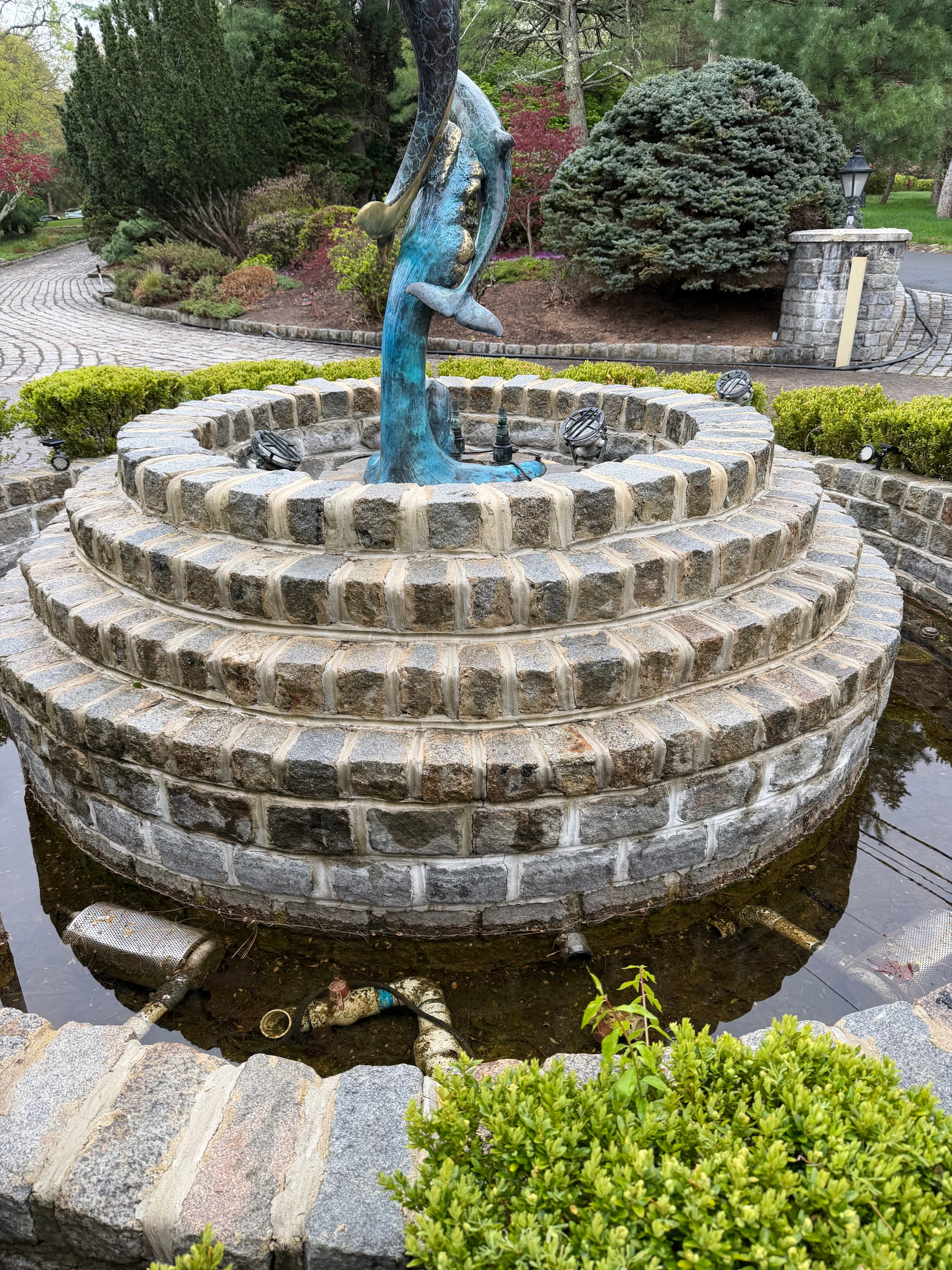 Circular natural stone fountain base with curved masonry walls in a landscaped garden.